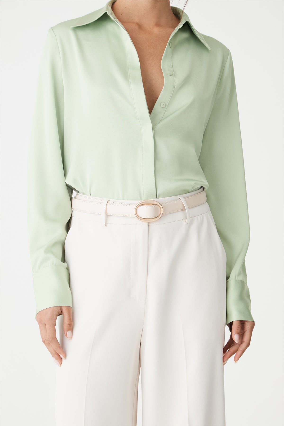 Detail of the mint satin shirt cuff and hem tucked into belted cream trousers