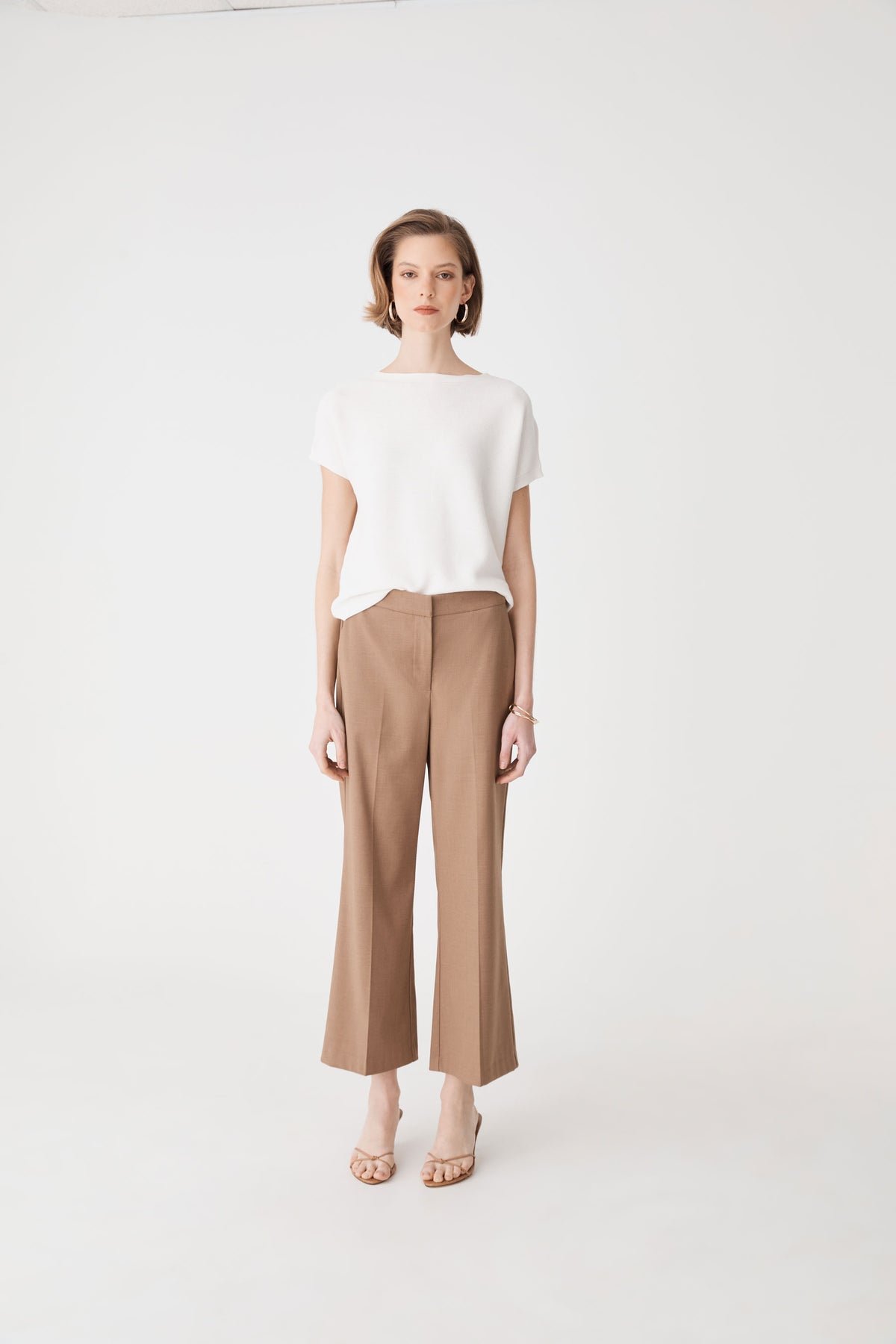 Full-length front view of the ivory knit top worn with tan wide-leg trousers