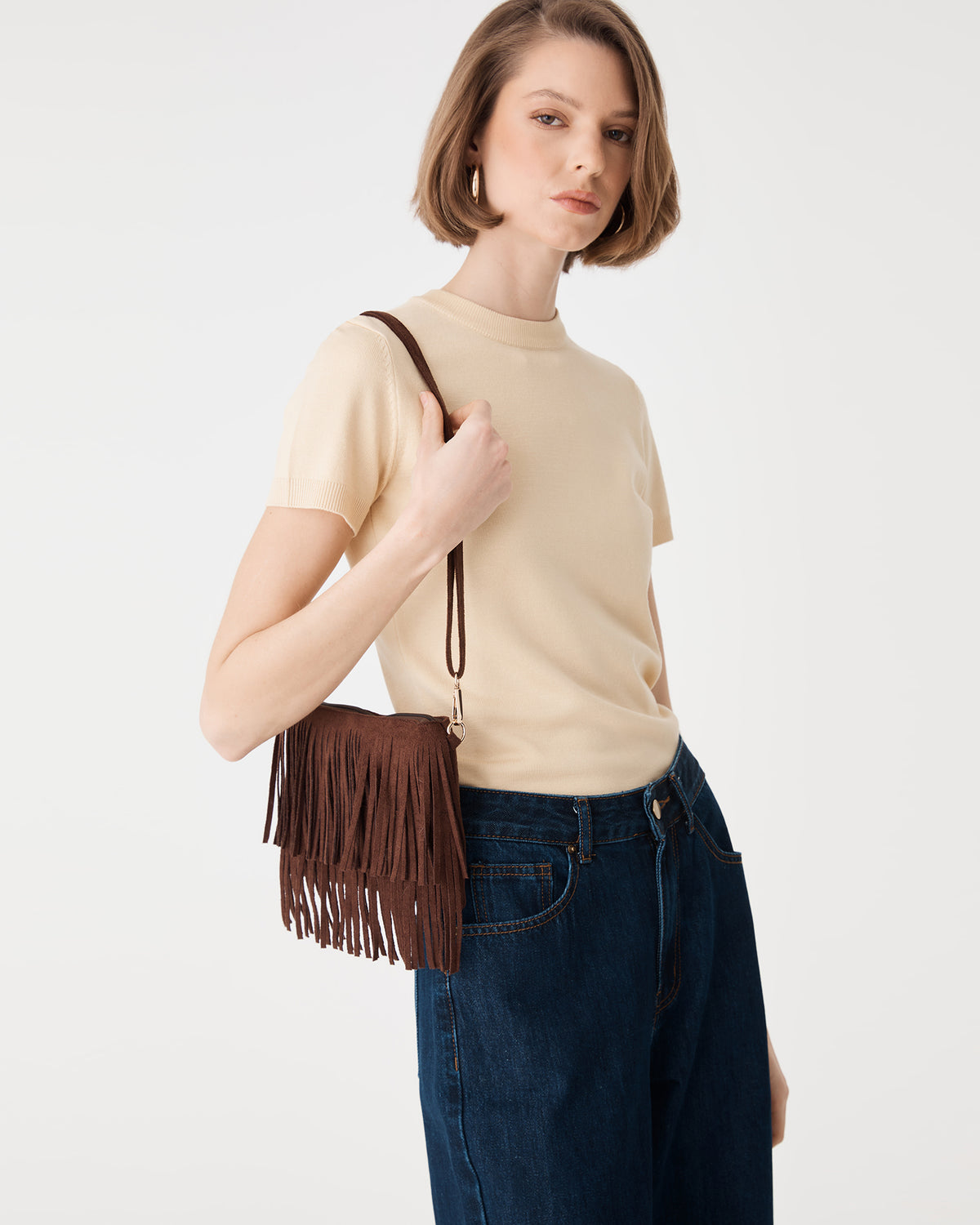 Tulum Fringe Bag in Chocolate Fondant held at the front, fringe detail with cream knit top and denim